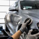 Detailer poleruje srebrny samochód za pomocą maszyny polerskiej w studiu auto detailingu