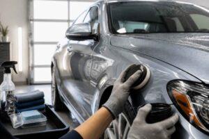 Detailer poleruje srebrny samochód za pomocą maszyny polerskiej w studiu auto detailingu